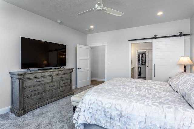 bedroom with a textured ceiling, a barn door, light colored carpet, and ceiling fan