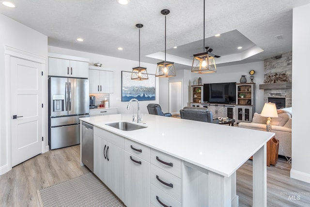 kitchen with stainless steel appliances, a raised ceiling, sink, a fireplace, and hanging light fixtures