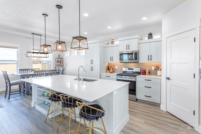 kitchen with sink, an island with sink, pendant lighting, white cabinets, and appliances with stainless steel finishes