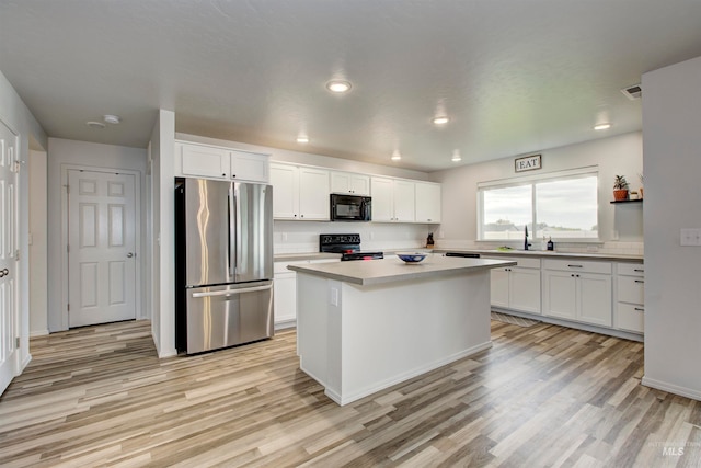 kitchen with white cabinetry, light hardwood / wood-style flooring, black appliances, and a center island