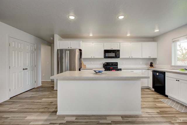 kitchen with light hardwood / wood-style floors, white cabinetry, black appliances, and a kitchen island