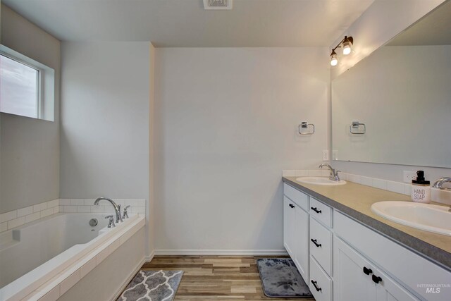 bathroom featuring vanity, wood-type flooring, and tiled bath