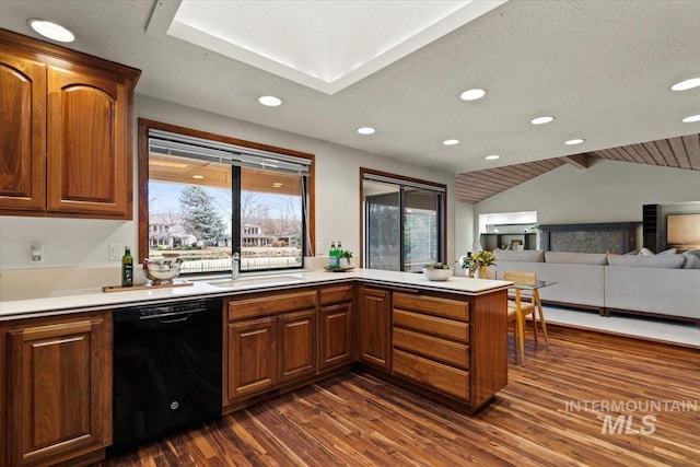 kitchen with dark wood finished floors, a peninsula, light countertops, vaulted ceiling, and black dishwasher