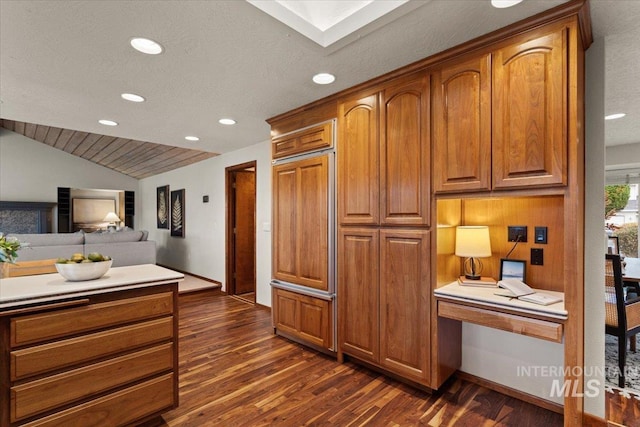 kitchen with vaulted ceiling, brown cabinets, dark wood-style flooring, and built in study area