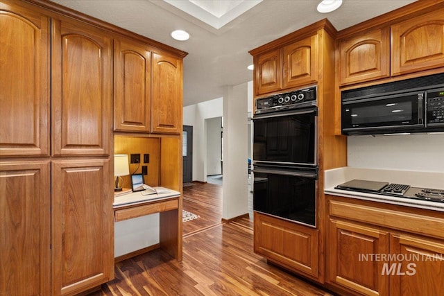 kitchen featuring black appliances, dark wood finished floors, brown cabinetry, and light countertops