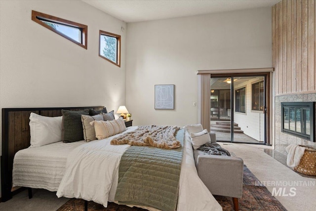 carpeted bedroom with a glass covered fireplace, a high ceiling, and access to outside