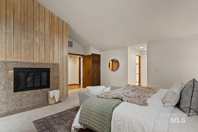 bedroom featuring visible vents, carpet flooring, a tiled fireplace, and vaulted ceiling