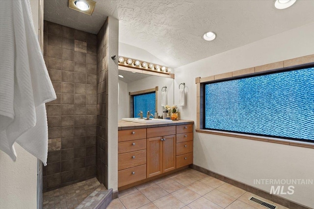 full bathroom featuring visible vents, a textured ceiling, vanity, and tiled shower