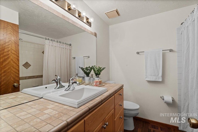 bathroom with visible vents, toilet, a textured ceiling, baseboards, and vanity