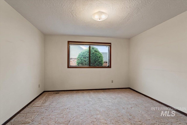 spare room with baseboards, light colored carpet, and a textured ceiling