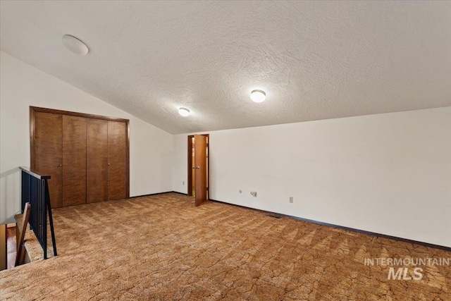 interior space featuring lofted ceiling, light colored carpet, baseboards, and a textured ceiling