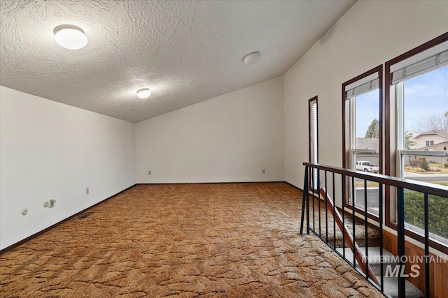 unfurnished room featuring baseboards, carpet, lofted ceiling, and a textured ceiling