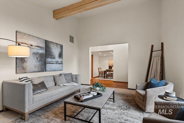 living room with beam ceiling, visible vents, a towering ceiling, and wood finished floors