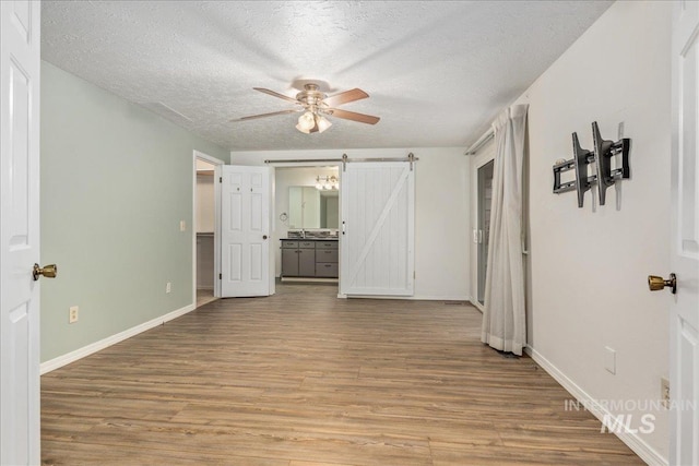 empty room with ceiling fan, a barn door, light hardwood / wood-style floors, and a textured ceiling