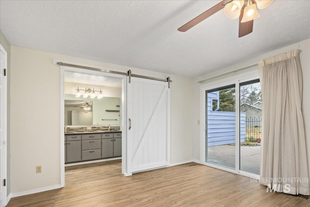 unfurnished bedroom featuring light hardwood / wood-style flooring, sink, access to outside, and a barn door