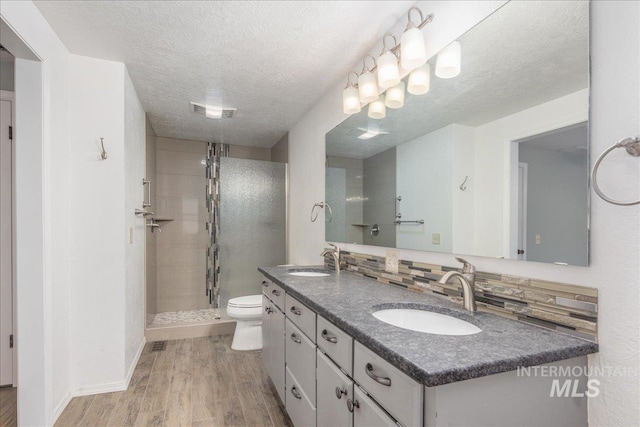 bathroom featuring wood-type flooring, vanity, walk in shower, toilet, and a textured ceiling