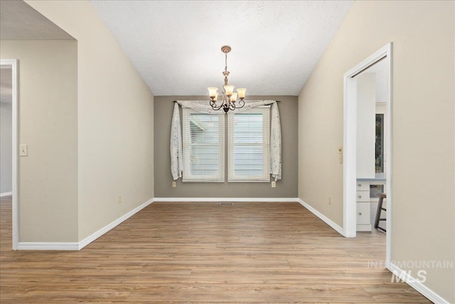 unfurnished dining area with a notable chandelier, a textured ceiling, and light hardwood / wood-style flooring