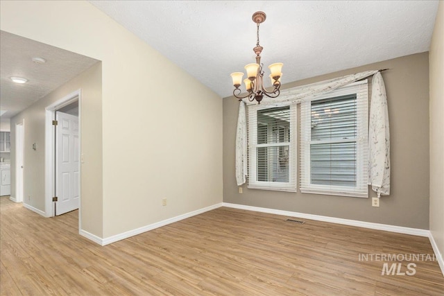 empty room with a textured ceiling, a notable chandelier, and light wood-type flooring