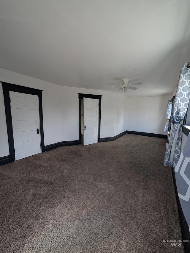 spare room featuring dark colored carpet, baseboards, and ceiling fan