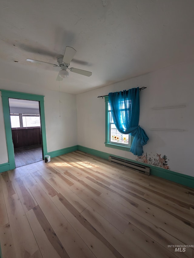 empty room featuring baseboards, a baseboard radiator, a ceiling fan, and hardwood / wood-style floors