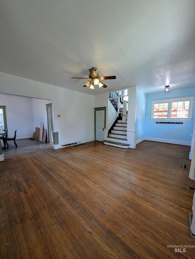 unfurnished living room featuring dark wood-type flooring, baseboards, and stairway