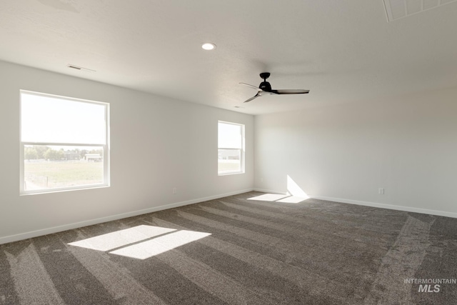 spare room with dark colored carpet, a ceiling fan, visible vents, and baseboards