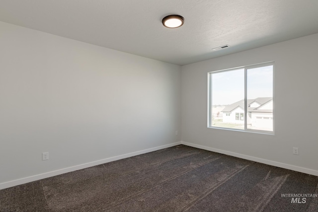 spare room featuring dark colored carpet, visible vents, and baseboards