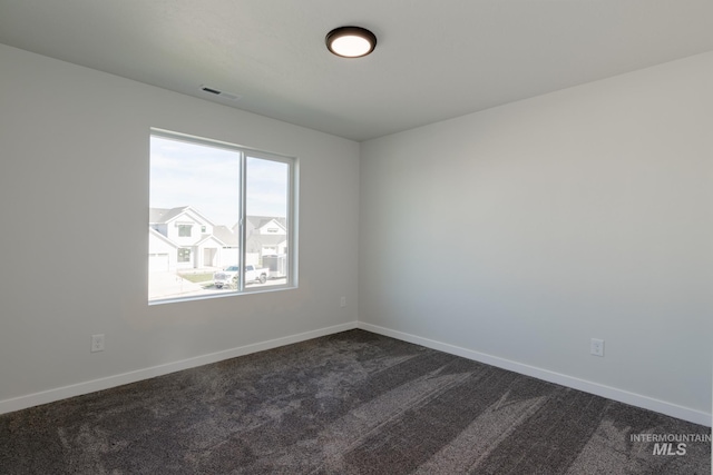 unfurnished room with dark colored carpet, visible vents, and baseboards