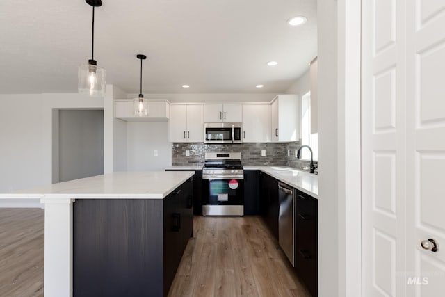 kitchen featuring decorative backsplash, appliances with stainless steel finishes, white cabinets, a sink, and a kitchen island