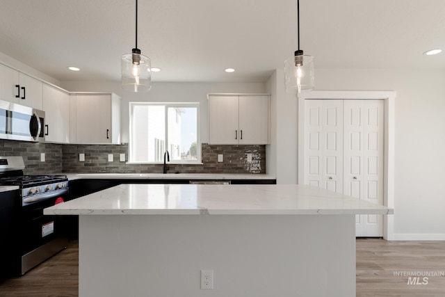 kitchen featuring light stone counters, stainless steel appliances, light wood-style floors, tasteful backsplash, and pendant lighting