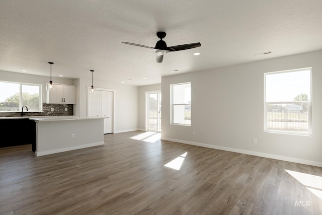 unfurnished living room featuring a textured ceiling, wood finished floors, a ceiling fan, and baseboards