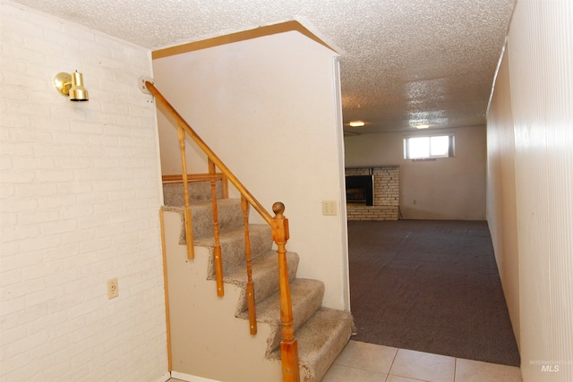 stairs featuring tile patterned flooring, a textured ceiling, brick wall, and a fireplace