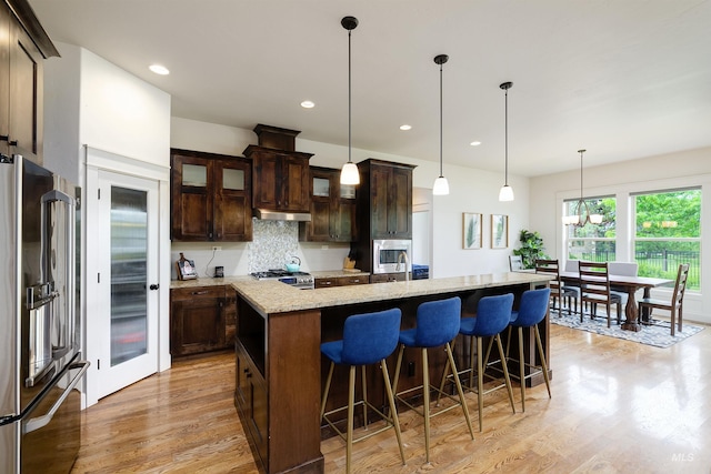 6859 N Topaz Jewel Pl, Meridian, ID 83646 - kitchen featuring appliances with stainless steel finishes, light wood-type flooring, backsplash, dark brown cabinets, and a center island with sink