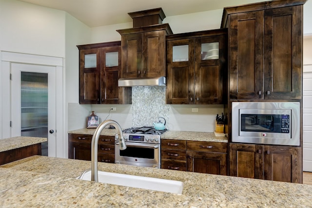 6859 N Topaz Jewel Pl, Meridian, ID 83646 - kitchen with stainless steel appliances, under cabinet range hood, dark brown cabinets, glass insert cabinets, and light stone counters