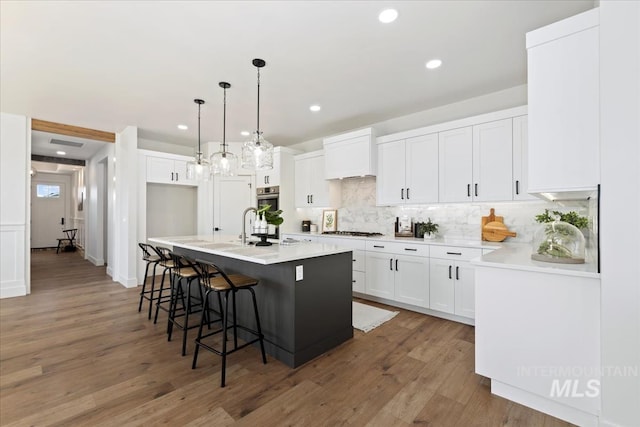 kitchen featuring decorative light fixtures, white gas stovetop, hardwood / wood-style floors, a kitchen island with sink, and white cabinets