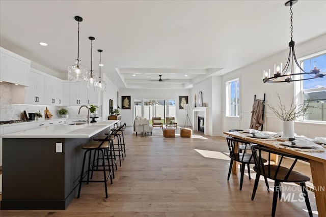 kitchen with sink, white cabinetry, a tray ceiling, a kitchen bar, and decorative light fixtures