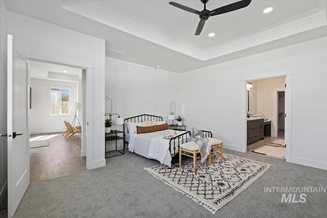 bedroom with ensuite bath, ceiling fan, ornamental molding, light carpet, and a raised ceiling