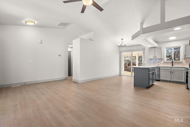 unfurnished living room featuring lofted ceiling, visible vents, light wood-style flooring, baseboards, and ceiling fan with notable chandelier