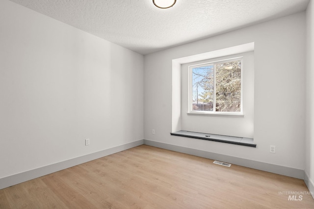 empty room featuring light wood finished floors, baseboards, visible vents, and a textured ceiling