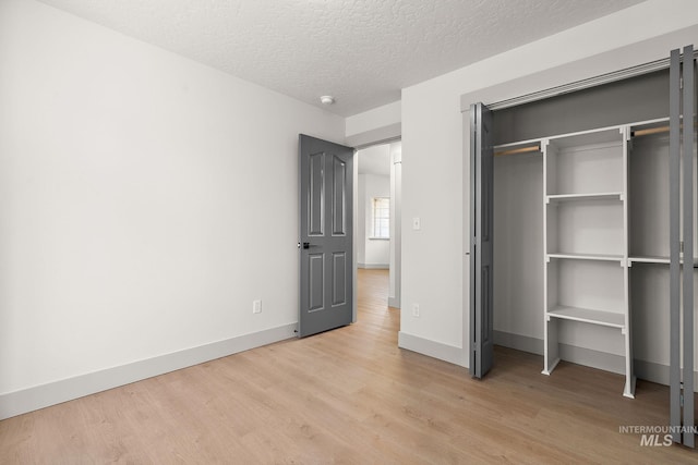 unfurnished bedroom featuring light wood-style floors, a closet, baseboards, and a textured ceiling