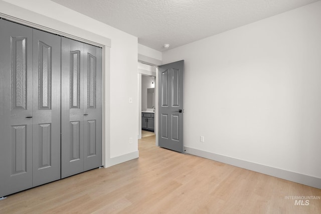 unfurnished bedroom featuring light wood-style flooring, a closet, baseboards, and a textured ceiling