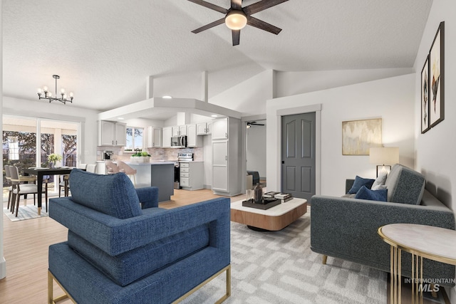 living room with vaulted ceiling, a textured ceiling, and ceiling fan with notable chandelier