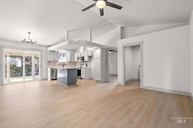 unfurnished living room with light wood finished floors, lofted ceiling, a textured ceiling, baseboards, and ceiling fan with notable chandelier