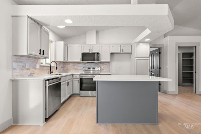 kitchen with lofted ceiling, a kitchen island, appliances with stainless steel finishes, light wood-type flooring, and a sink