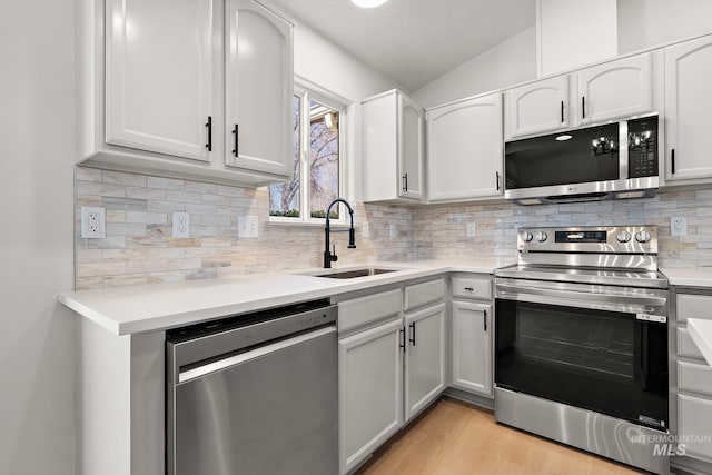 kitchen featuring light wood-style flooring, stainless steel appliances, a sink, vaulted ceiling, and tasteful backsplash