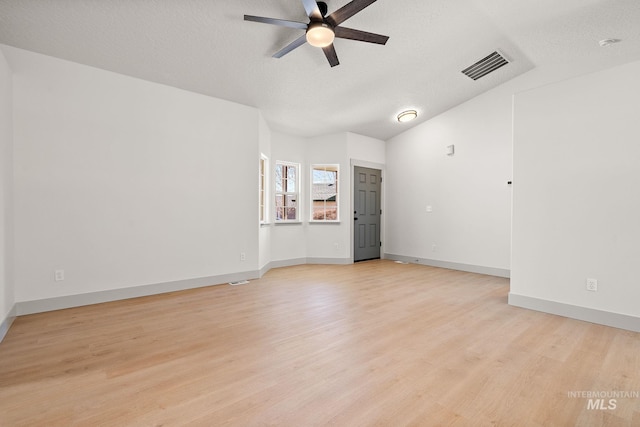 spare room featuring lofted ceiling, visible vents, light wood-style floors, a ceiling fan, and a textured ceiling