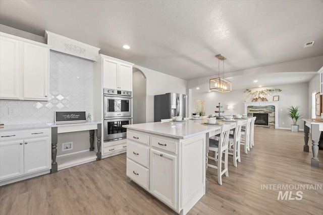 120 Pilgrim Way, Middleton, ID 83644 - kitchen with stainless steel appliances, a breakfast bar, a stone fireplace, white cabinets, and arched walkways