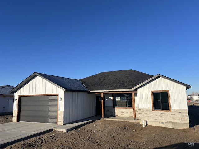 modern inspired farmhouse featuring roof with shingles, an attached garage, board and batten siding, stone siding, and driveway