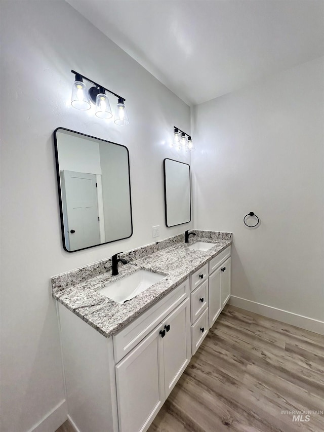 bathroom with double vanity, wood finished floors, a sink, and baseboards