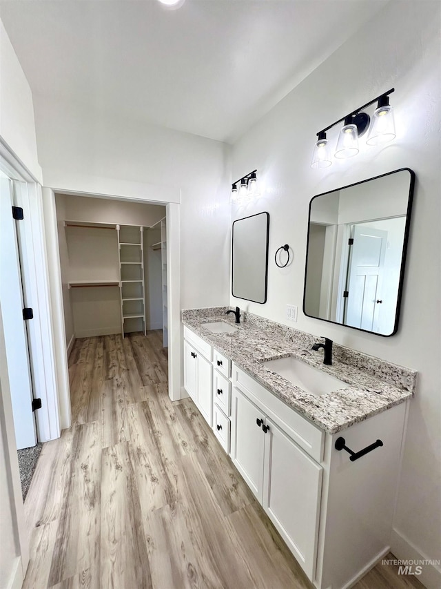 full bathroom featuring double vanity, a walk in closet, a sink, and wood finished floors